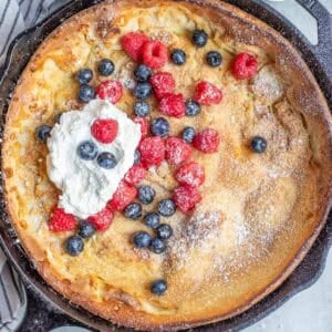 a cast iron skillet with a dutch baby pancake topped with fresh berries and whipped cream.