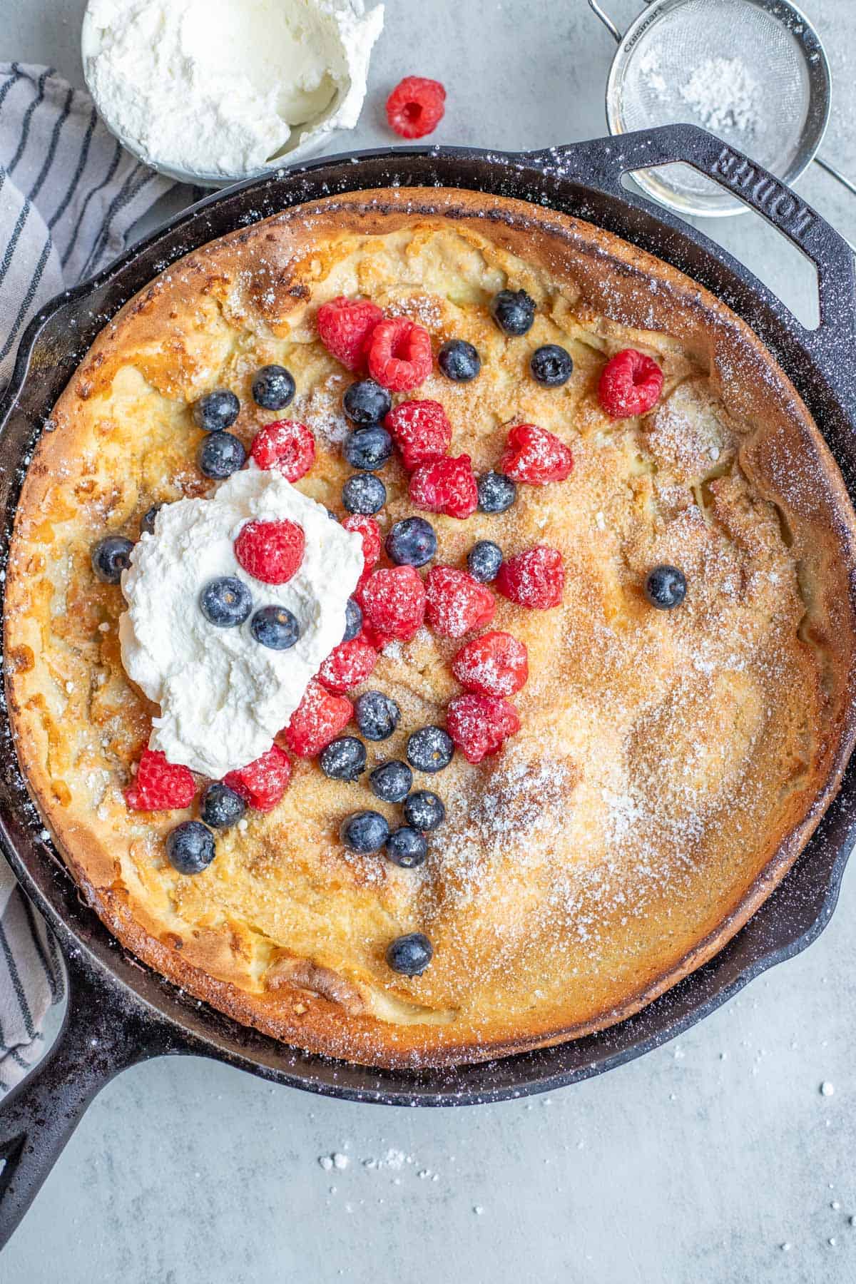 A cast iron skillet with a Dutch baby pancake topped with fresh berries and whipped cream.