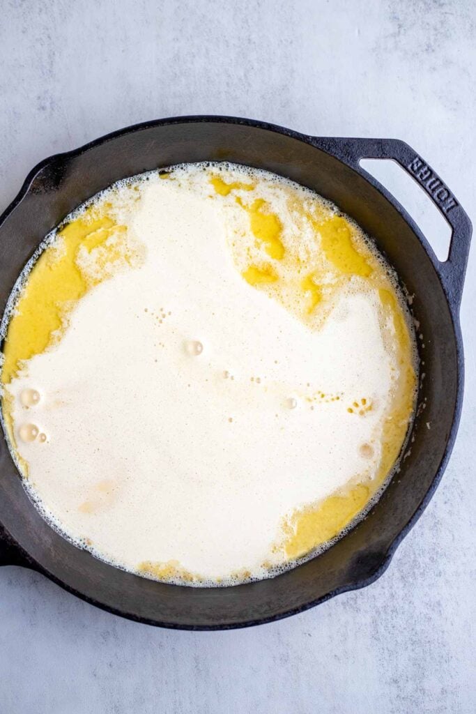 Melted butter and Dutch baby pancake batter poured into a cast iron skillet to bake.