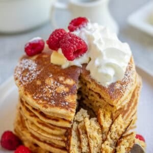 a stack of whole wheat pancakes topped with whipped cream and raspberries.