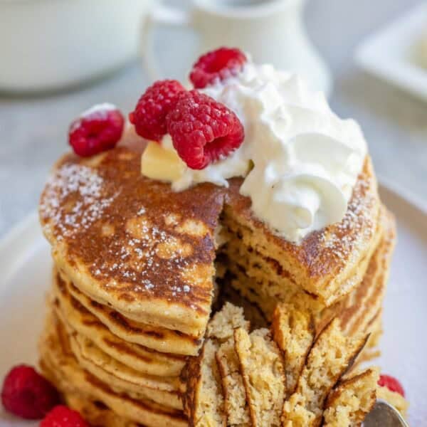 a stack of whole wheat pancakes topped with whipped cream and raspberries.