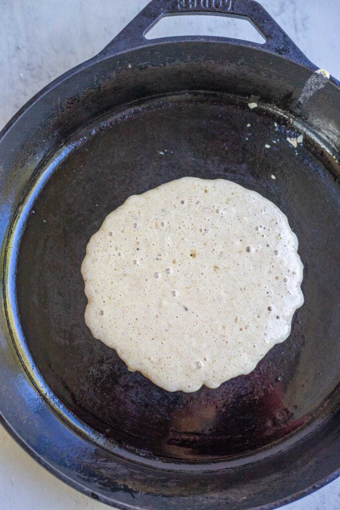 A pancake cooking in a cast iron skillet with butter.