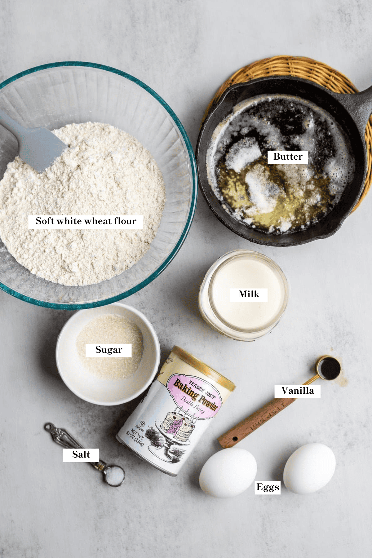 Whole wheat flour, butter, milk, sugar, eggs, vanilla, and baking powder on the kitchen counter.