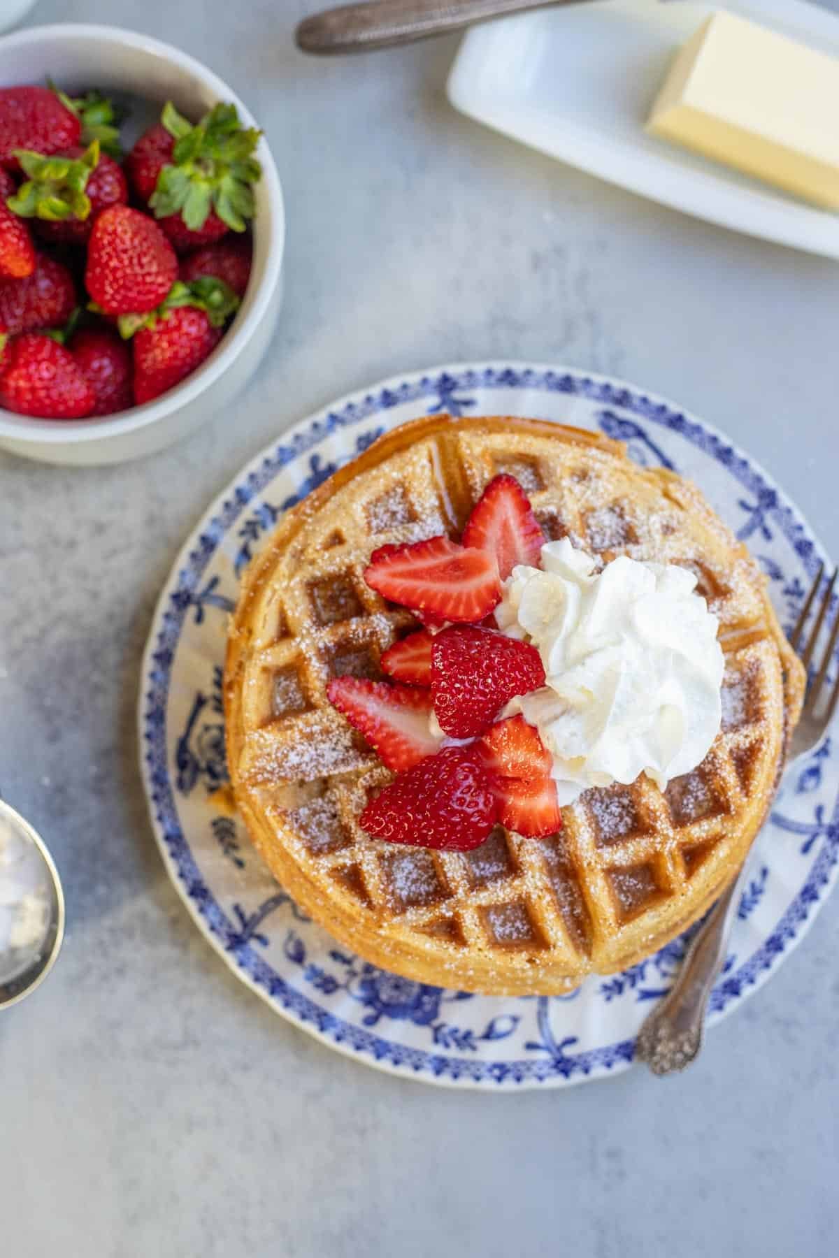 An overhead view of whole wheat waffles topped with whipped cream and strawberries.