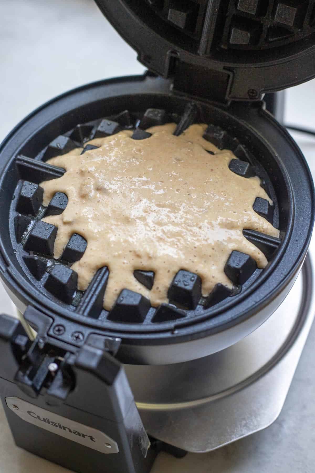 One cup of the waffle batter poured onto a waffle maker.