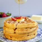 syrup being poured over a stack of whole wheat waffles.