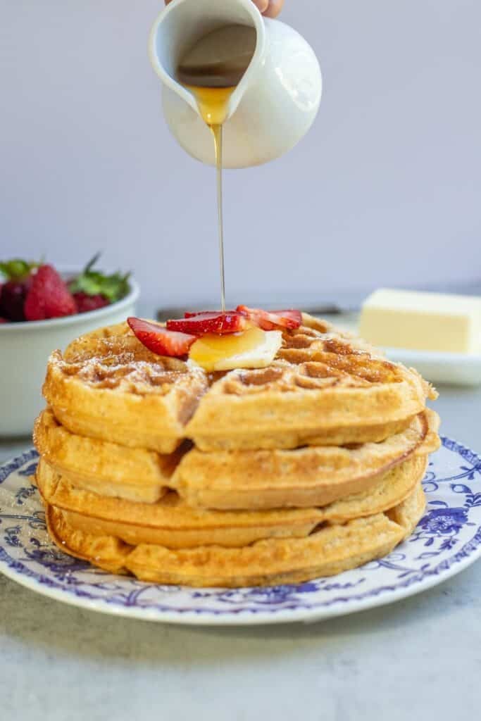 Syrup being poured over a stack of whole wheat waffles.