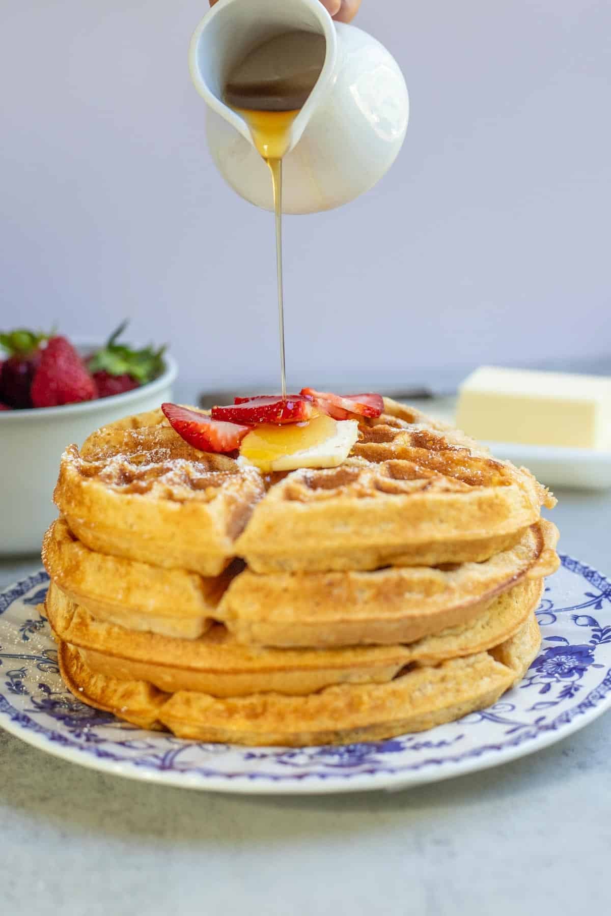 Syrup being poured over a stack of whole wheat waffles.