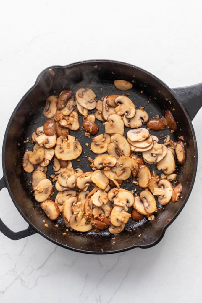 Sliced mushrooms in a cast iron skillet with melted butter.