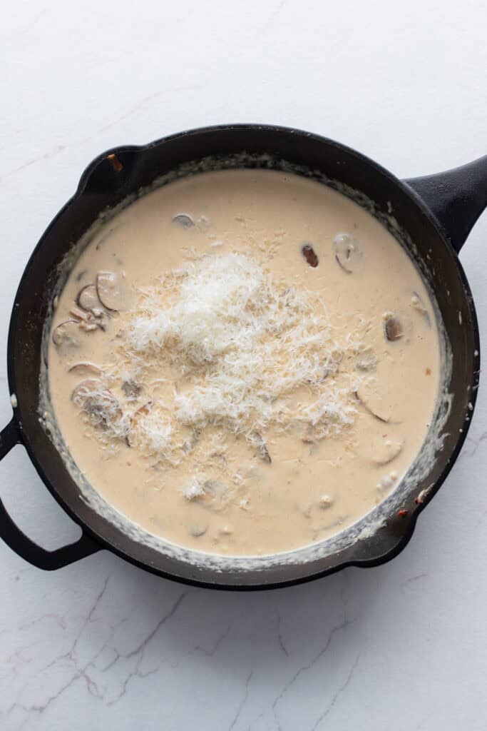 Parmesan cheese in a cast iron skillet with mushrooms and cream to make a sauce.