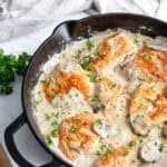 Chicken breast and garnishes added into the mushroom cream sauce in a cast iron skillet.