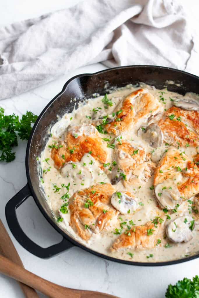 Chicken breast and garnishes added into the mushroom cream sauce in a cast iron skillet.