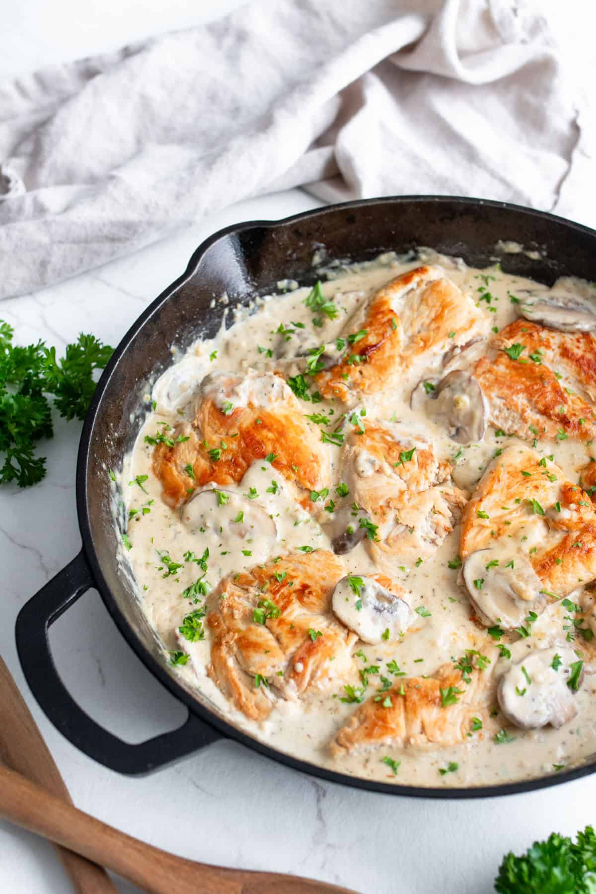 Chicken breast and garnishes added into the mushroom cream sauce in a cast iron skillet.