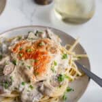 pasta noodles covered in a creamy chicken and mushroom sauce on a cream colored plate.