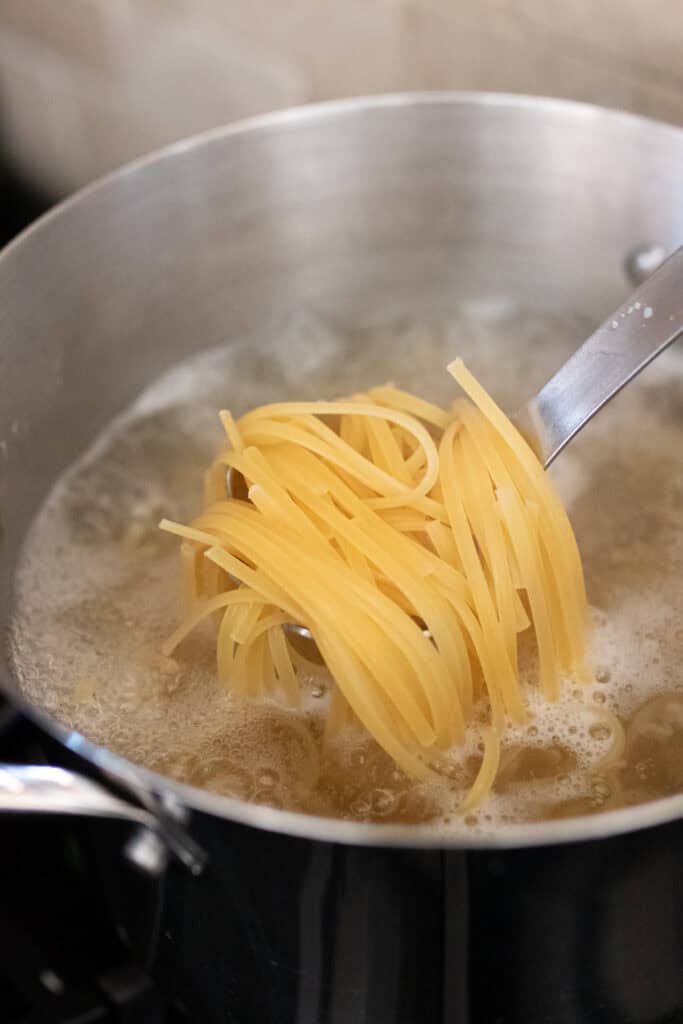 A ladle filled with pasta over a pot of boiling water.