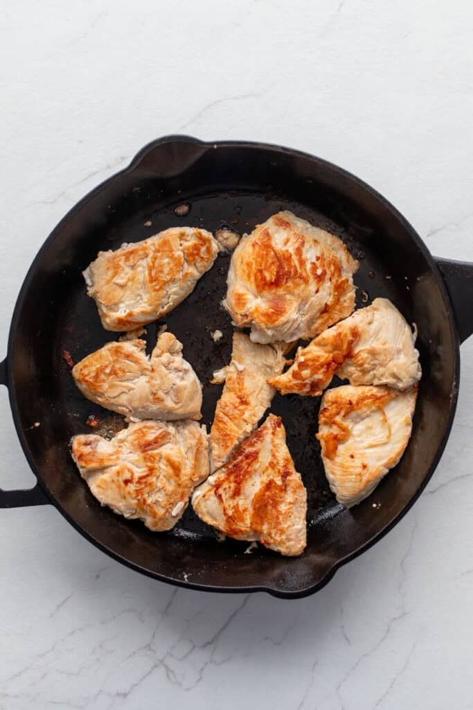 Chicken breasts browned in a cast iron skillet.