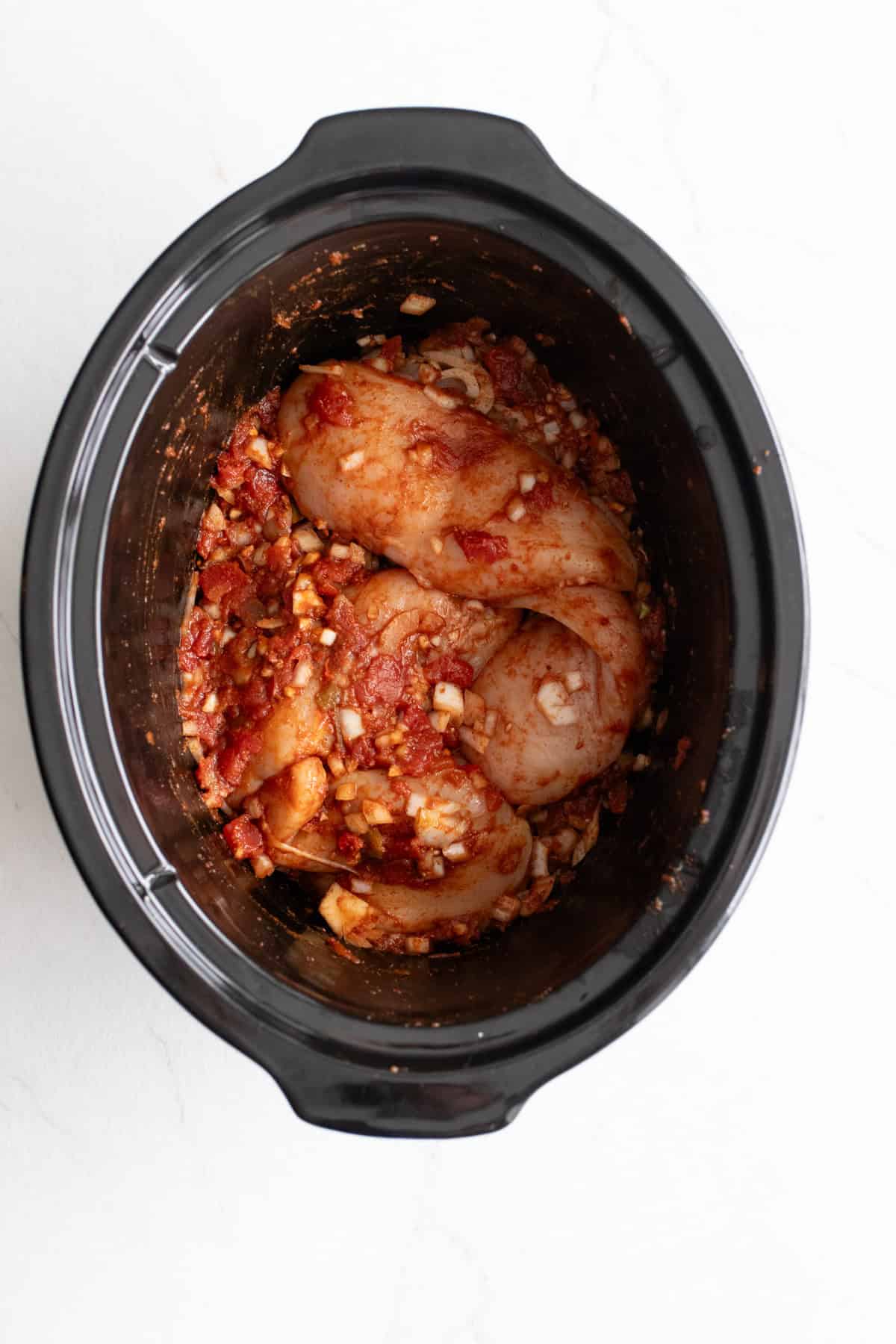 Chicken breast in a crockpot mixed with seasoning.