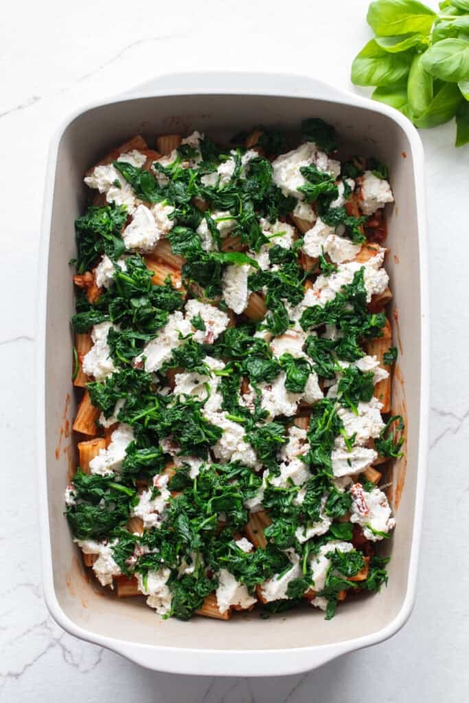 Spinach on top of pasta in a casserole dish.