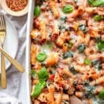 Baked ziti in a casserole dish next to a few utensils.