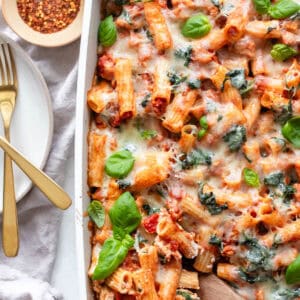 Baked ziti in a casserole dish next to a few utensils.