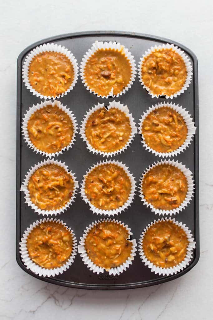 A muffin tin filled lined with muffin liners and filled 3/4 way full with muffin mixture.