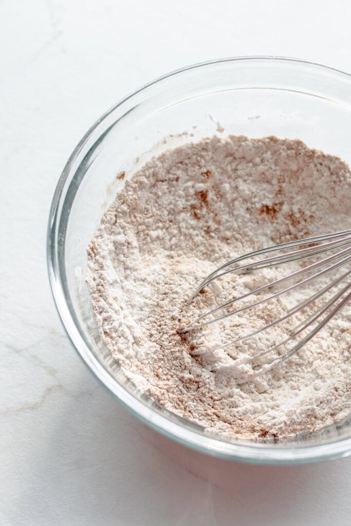 Flour, baking soda, salt, and cinnamon whisked together in a glass bowl.