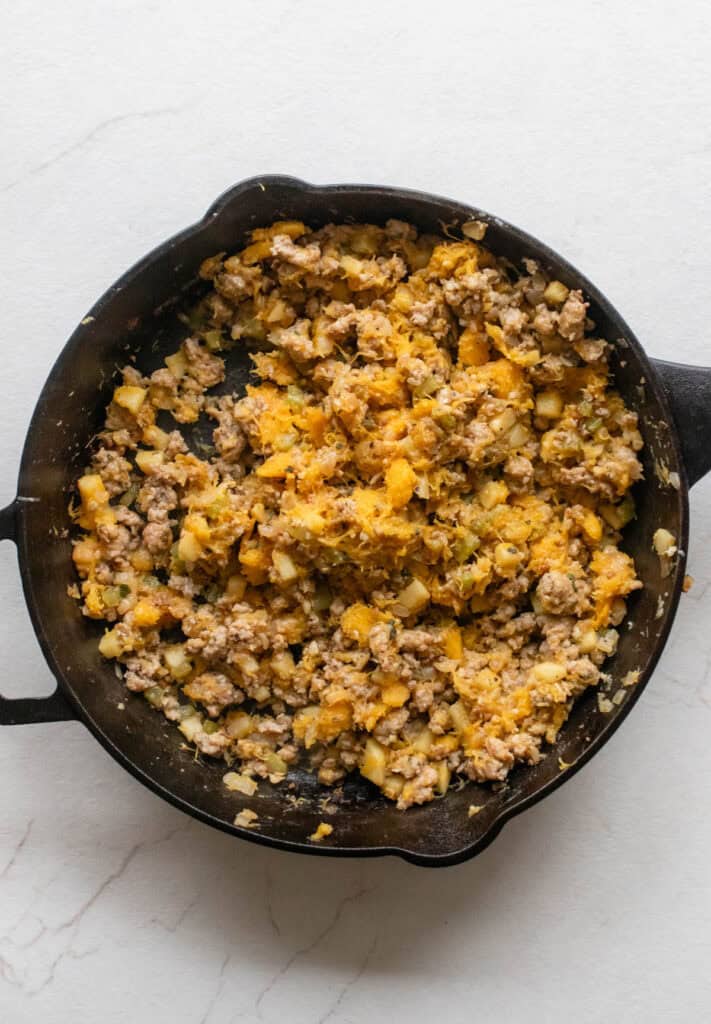 Squash flesh added to sausage in a cast iron skillet.