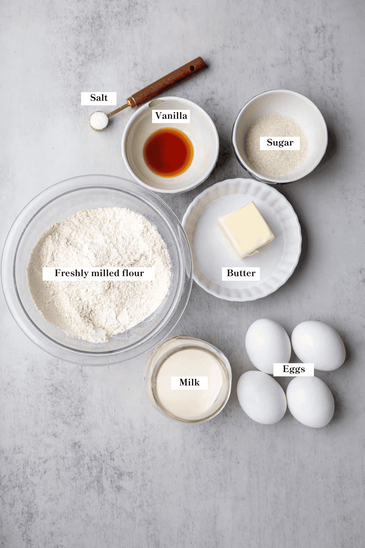 Eggs, butter, flour, milk, sugar, vanilla, and salt on the kitchen counter.