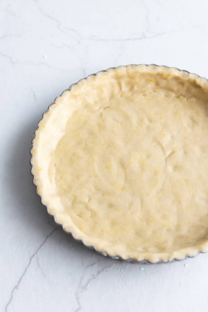 Tart dough pressed firmly in a tart pan on a kitchen counter.