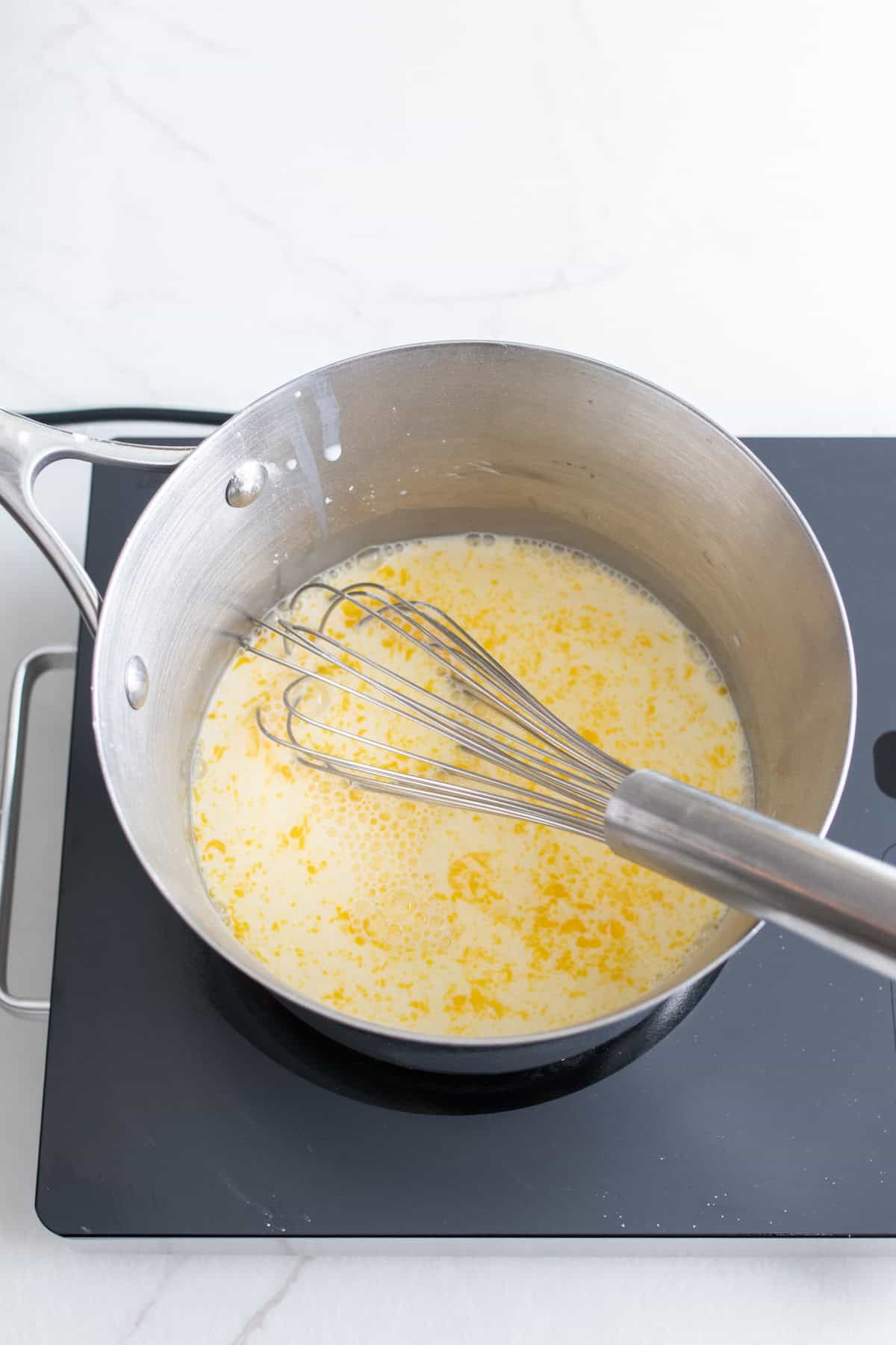 Ingredients to make a custard being whisked in a pot on the stove.