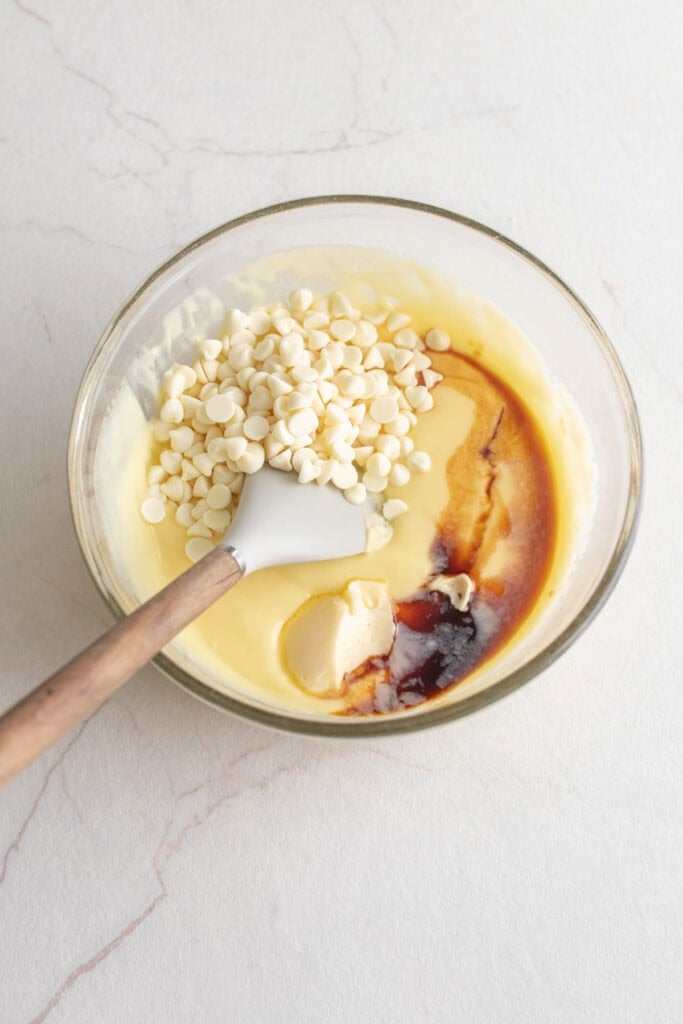 Strained custard with vanilla and white chocolate chips in a glass mixing bowl.