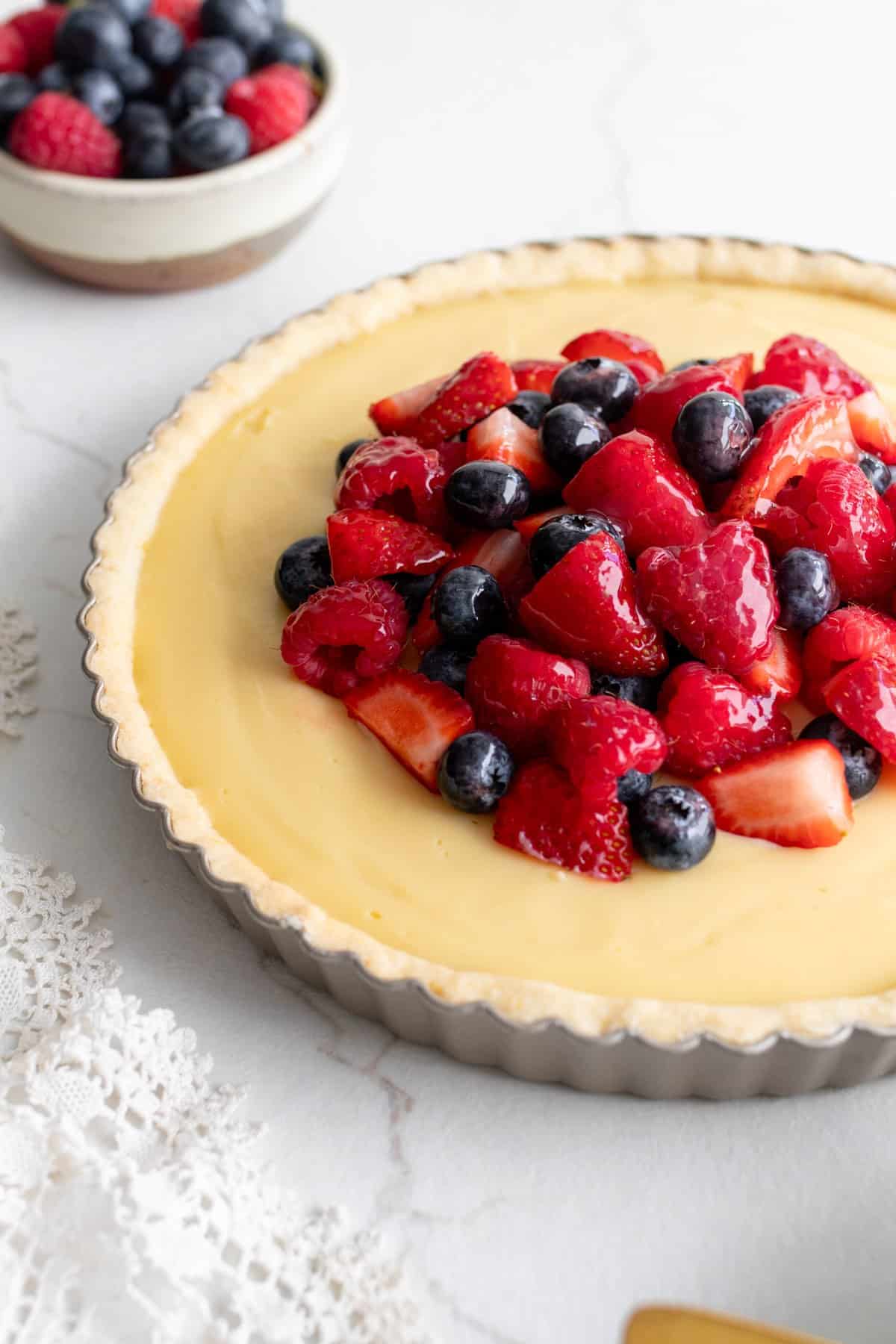 A tart pan filled with a white chocolate custard topped with a mixed berry compote.