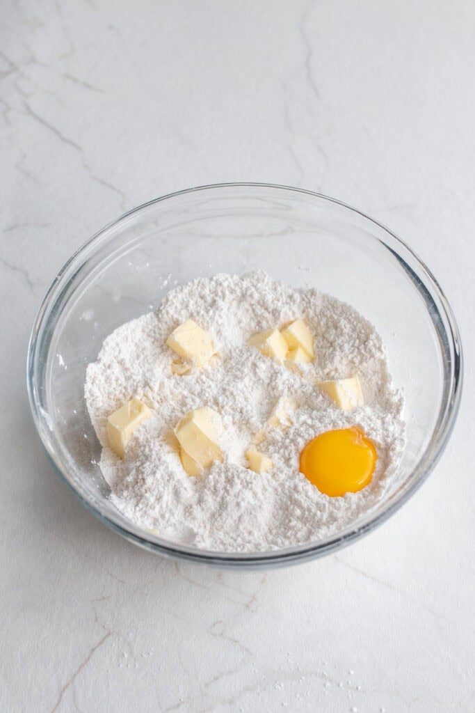 Flour, sugar, cold butter cubes, and eggs in a glass mixing bowl.