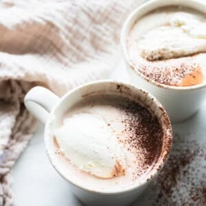 a white mug full of bone broth hot chocolate topped with whipped cream and a dash of cinnamon.