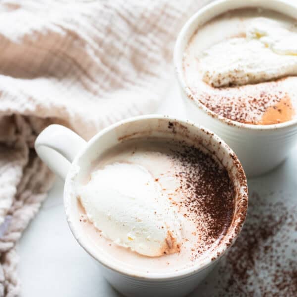 a white mug full of bone broth hot chocolate topped with whipped cream and a dash of cinnamon.