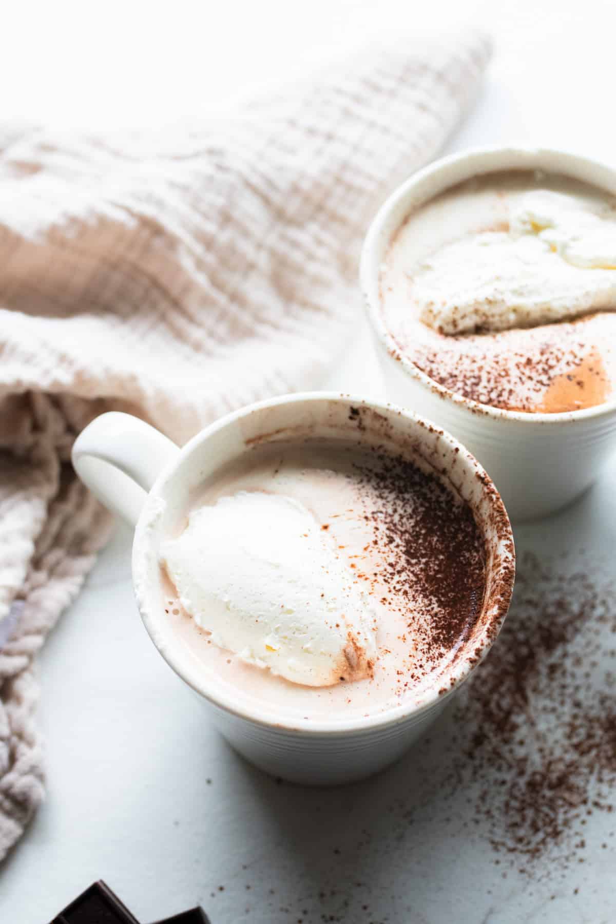 A white mug full of bone broth hot chocolate topped with whipped cream and a dash of cinnamon.