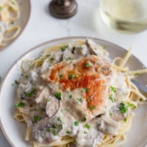 pasta on a serving plate topped with a mushroom cream sauce and a cooked chicken breast.