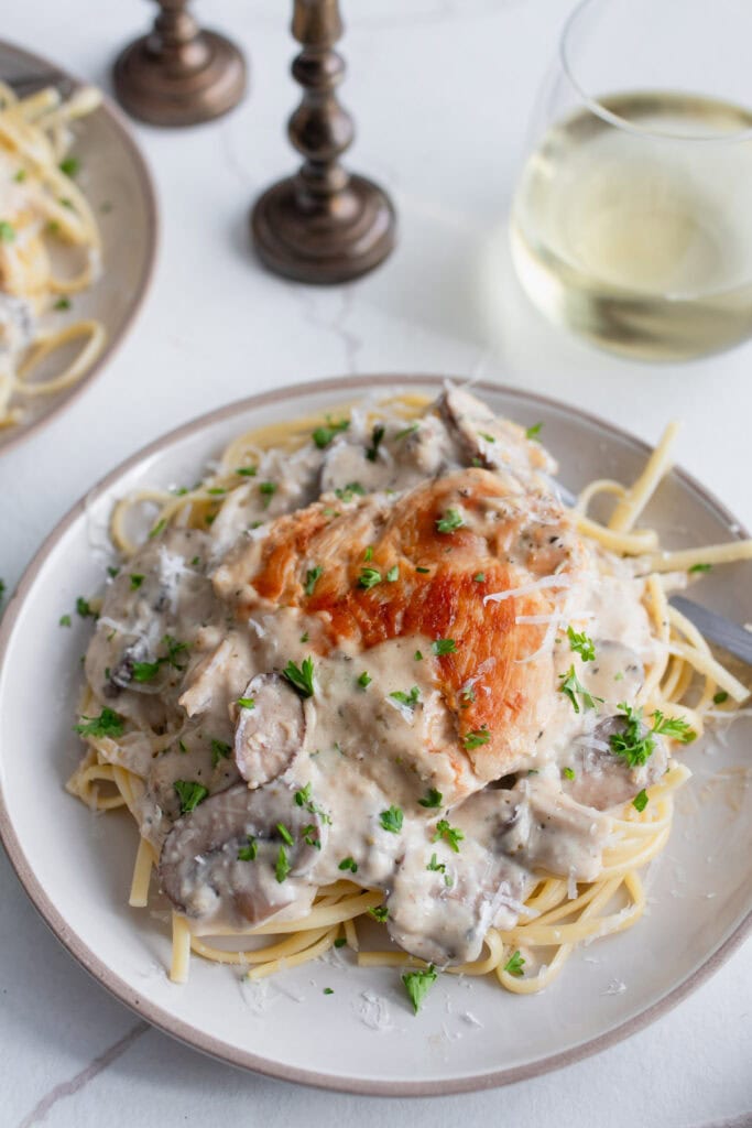 Pasta on a serving plate topped with a mushroom cream sauce and a cooked chicken breast.