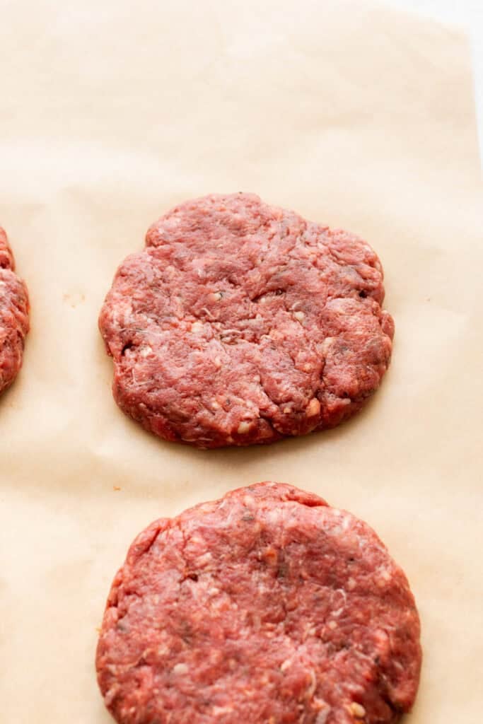 Raw, flattened beef patties on parchment paper.