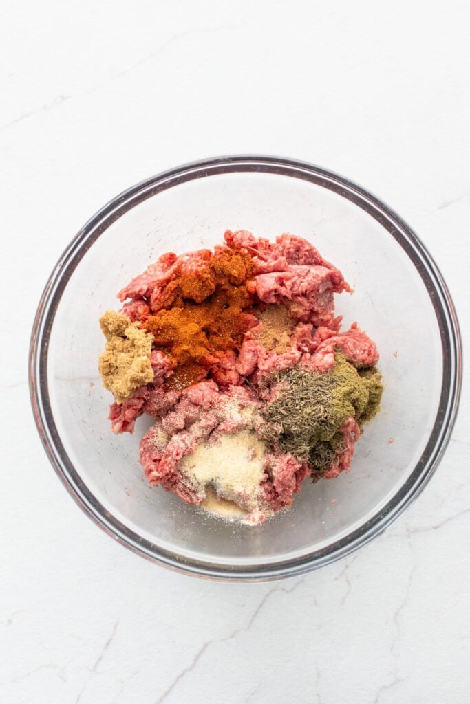 Ground beef with dried seasonings in a bowl.