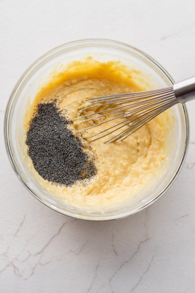 Poppy seeds added to a batter in a bowl.