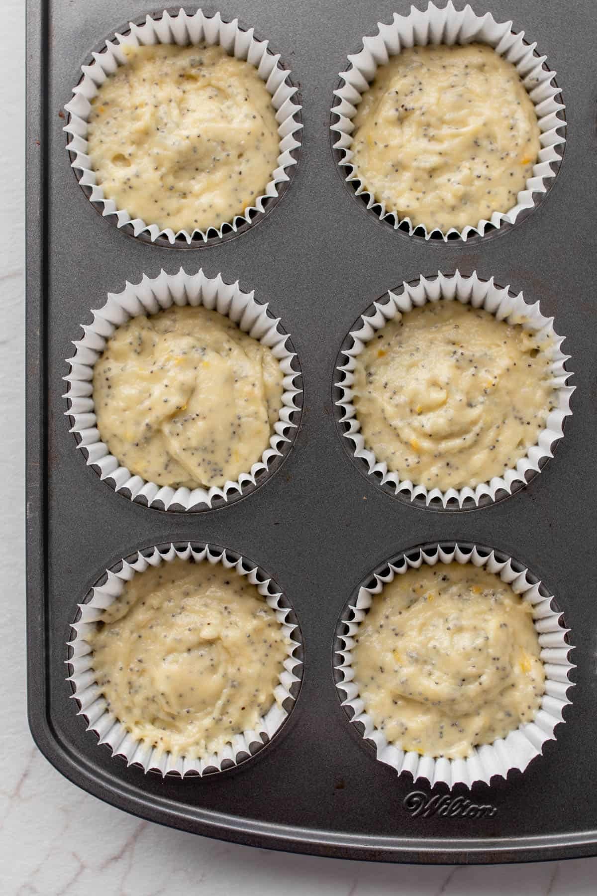 Lemon poppyseed muffin batter in a muffin tin.
