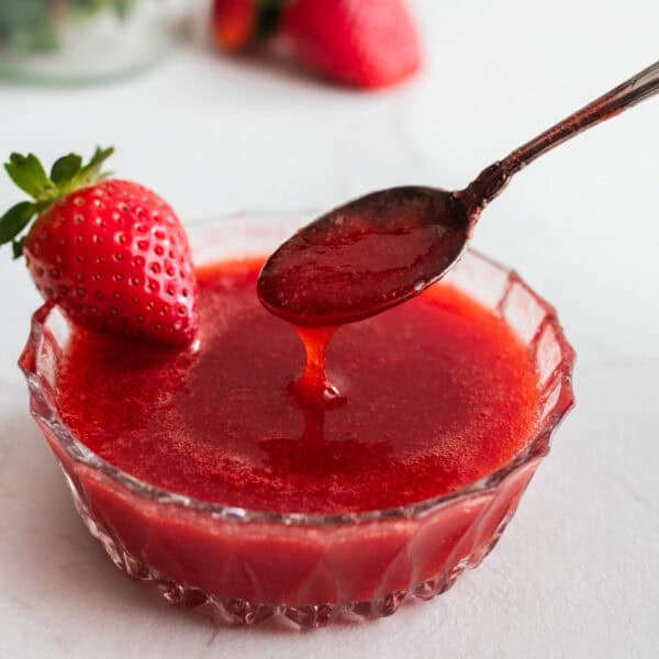 A bowl of strawberry sauce with a spoon.