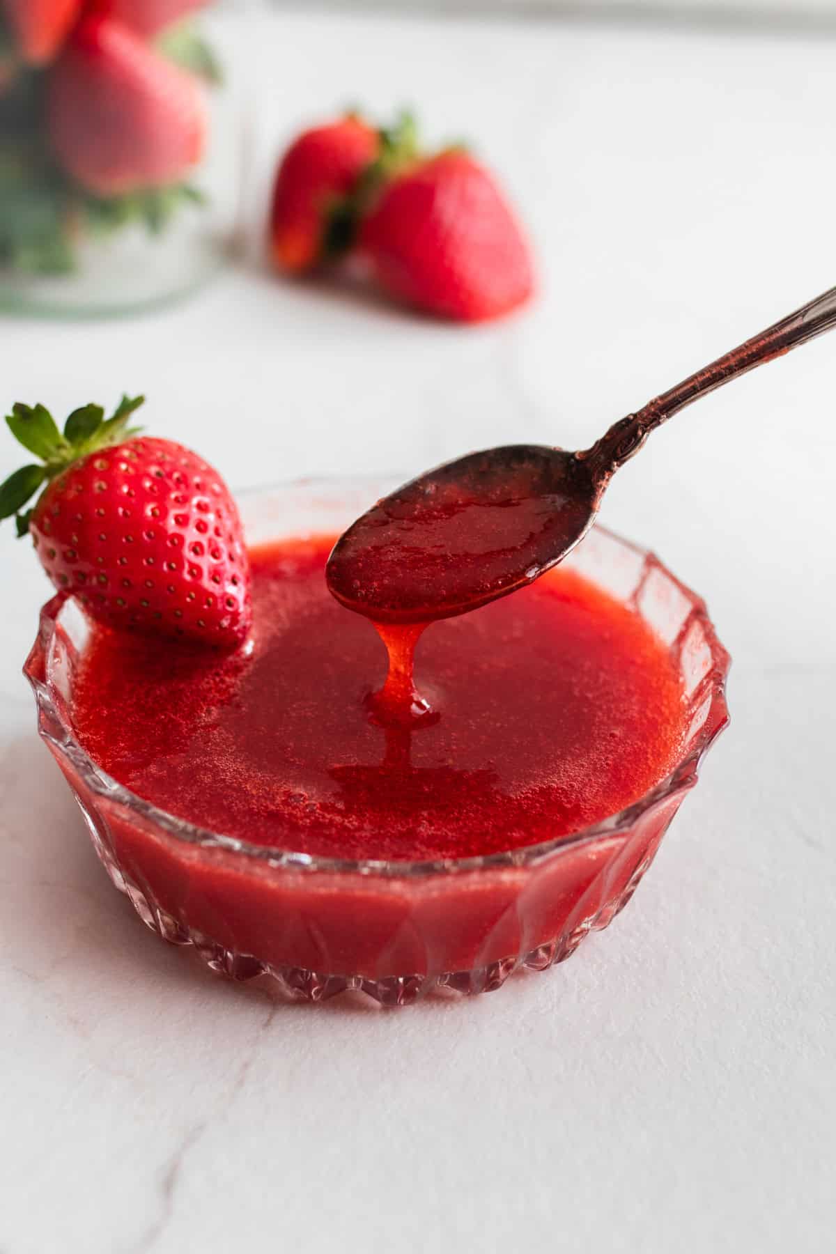 A bowl of strawberry sauce with a spoon.