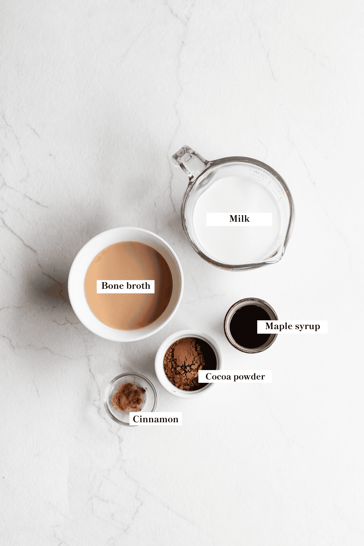 Milk, bone broth, maple syrup, cocoa powder, and cinnamon on the counter.
