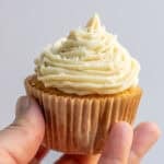 a woman's hand holding a vanilla cupcake piped with vanilla buttercream frosting.