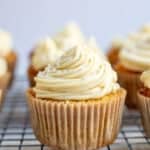 a vanilla cupcake piped with buttercream frosting on a wire cooling wrack.