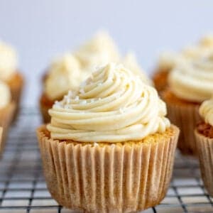 a vanilla cupcake piped with buttercream frosting on a wire cooling wrack.