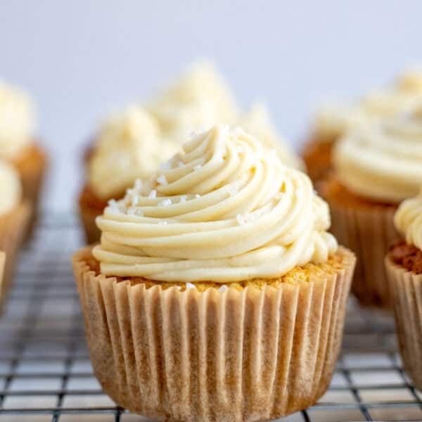 a vanilla cupcake piped with buttercream frosting on a wire cooling wrack.