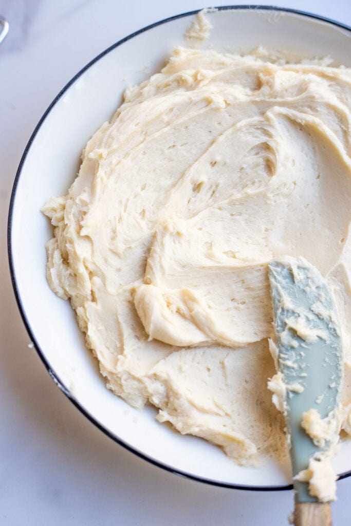 A white dessert plate with butter cream frosting spread with a small spatula.